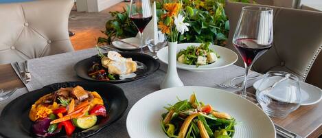 A dining table with three plates of food, a vase with flowers, and wine glasses.