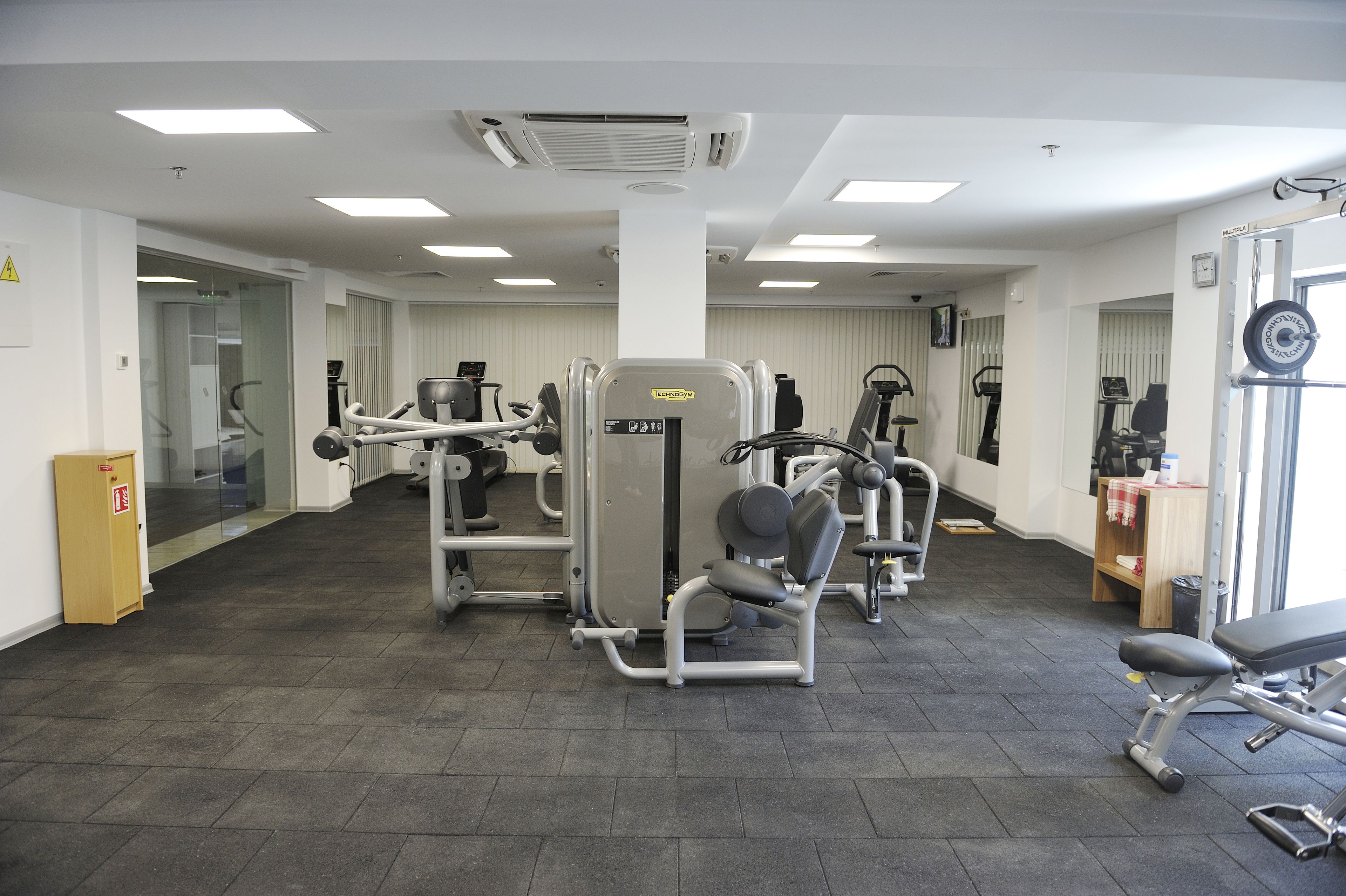 A gym with various exercise machines, a bench, and a door leading to another room.