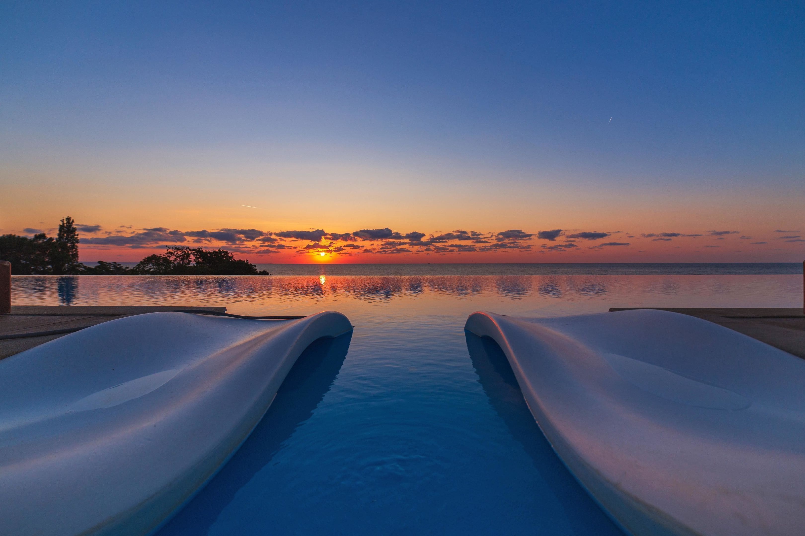 Ein Pool mit zwei Rutschen bei Sonnenuntergang, der Himmel und Wasser spiegelt.