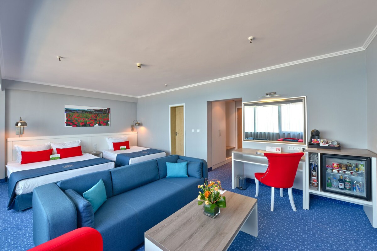 Une chambre d’hôtel avec deux lits, un canapé, un bureau, un miroir et un mini-bar.