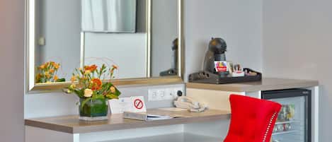 Une chambre d’hôtel équipée d’un bureau, d’une chaise rouge, d’un mini-bar, d’un miroir et d’un petit réfrigérateur.