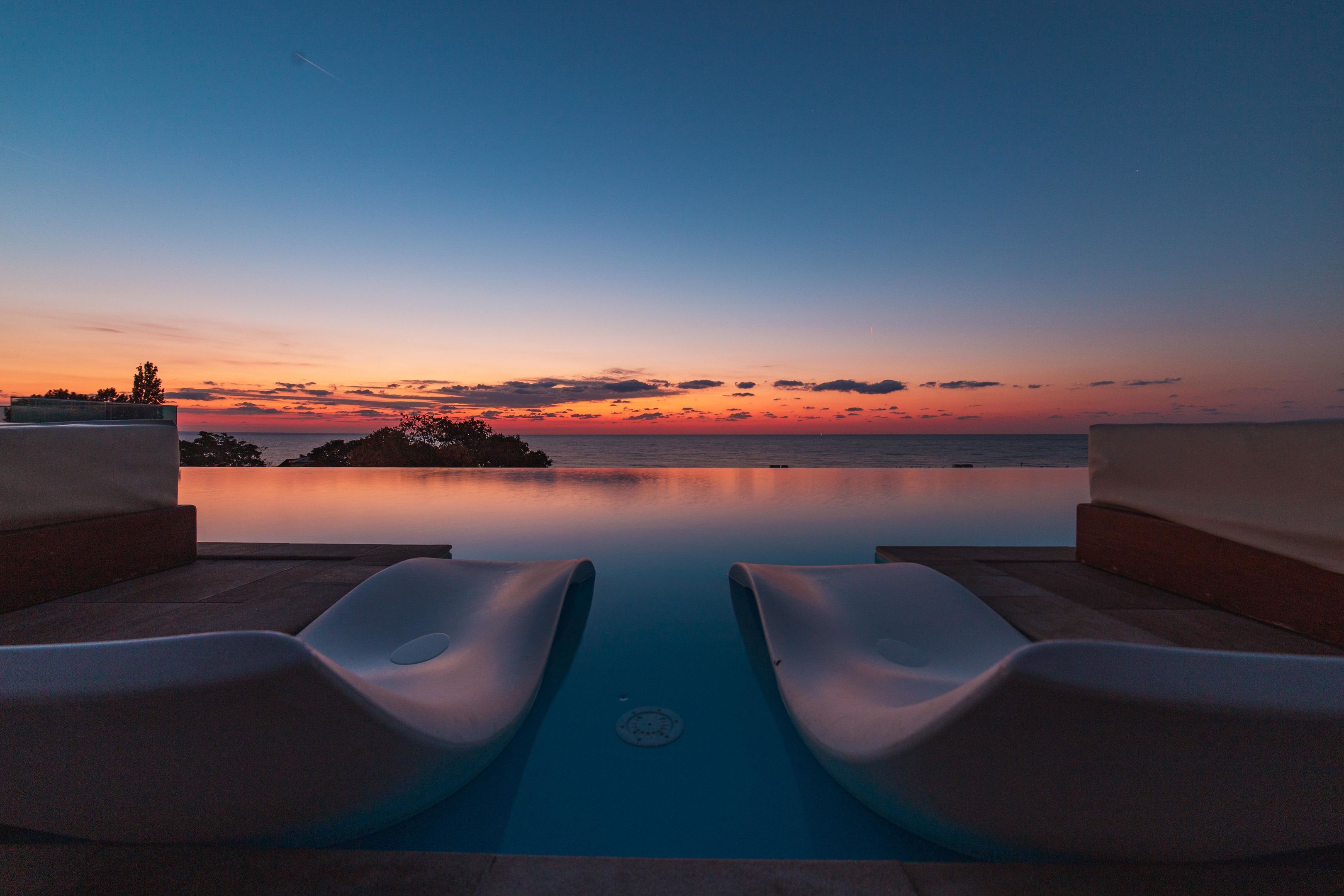 A poolside view with two lounge chairs and a sunset over the water.