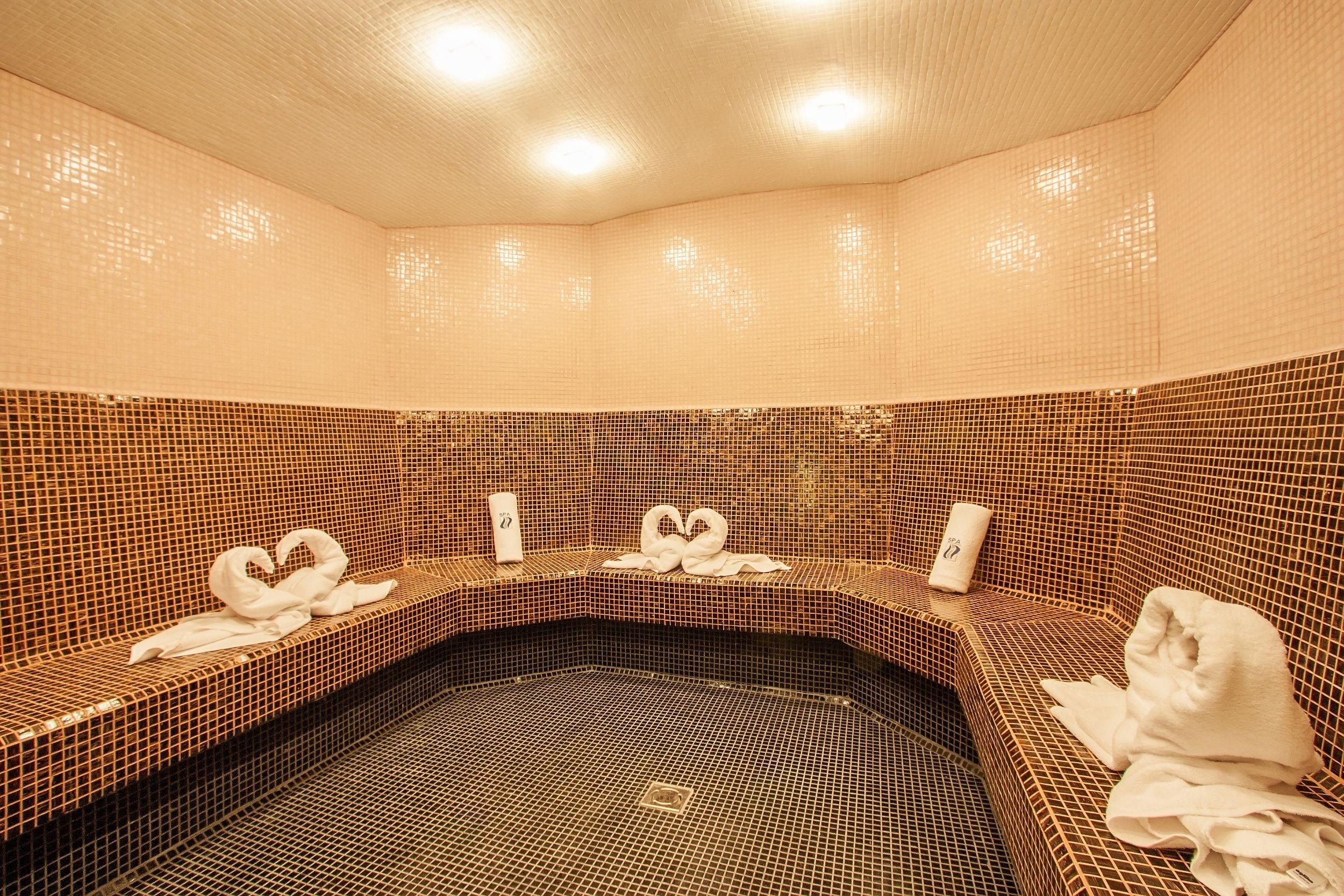 A spa area with tiled walls and benches, towels, and a bottle on the benches.