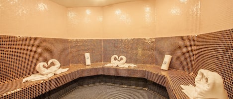 A spa area with tiled walls and benches, towels, and a bottle on the benches.