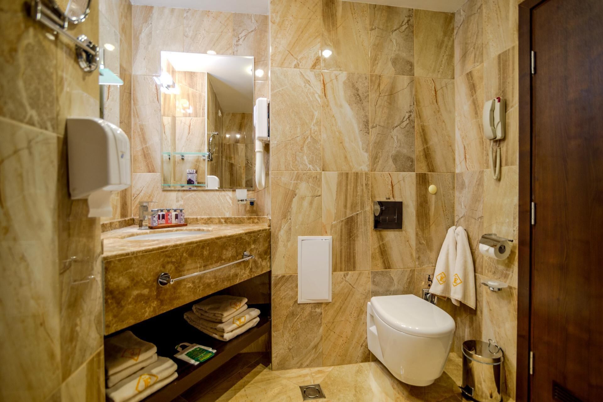 A bathroom with marble walls, a sink with a glass enclosure, a toilet, and a towel rack.