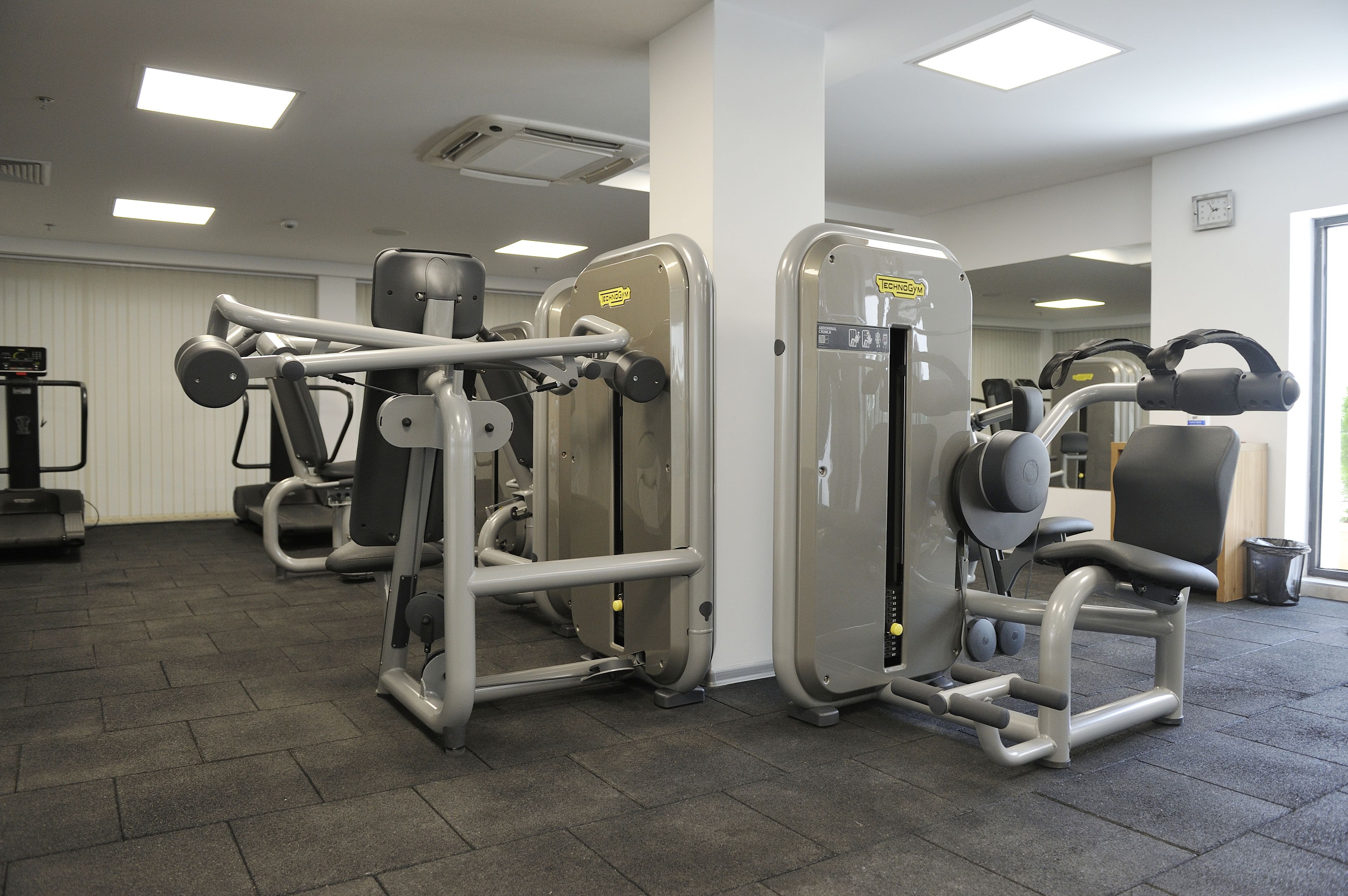 A gym with various exercise machines, a mirror, and a clock on the wall.