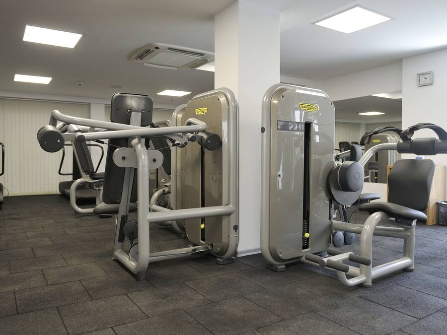 A gym with various exercise machines, a mirror, and a clock on the wall.