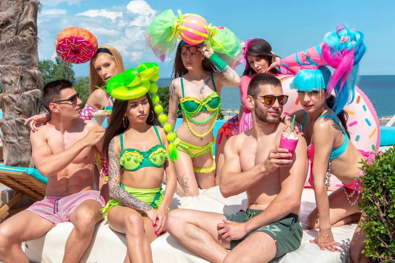 Un gruppo di persone sedute su una sedia da spiaggia, vestite con abiti da mare colorati e accessori.