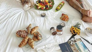 A bed with a tufted headboard, a breakfast spread including pastries, fruits, and beverages, and a laptop on the bed. - INTERNATIONAL Hotel Casino & Tower Suites (Golden Sands)