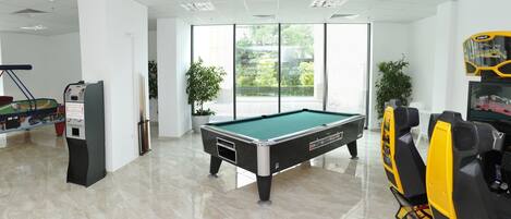 Una mesa de billar en una habitación bien iluminada con un gran ventanal, una mesa de billar y una mesa de billar con sistema de devolución de bolas.
