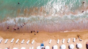 An aerial view of a beach with people swimming and sunbathing, and rows of sun loungers and umbrellas. - INTERNATIONAL Hotel Casino & Tower Suites (Golden Sands)