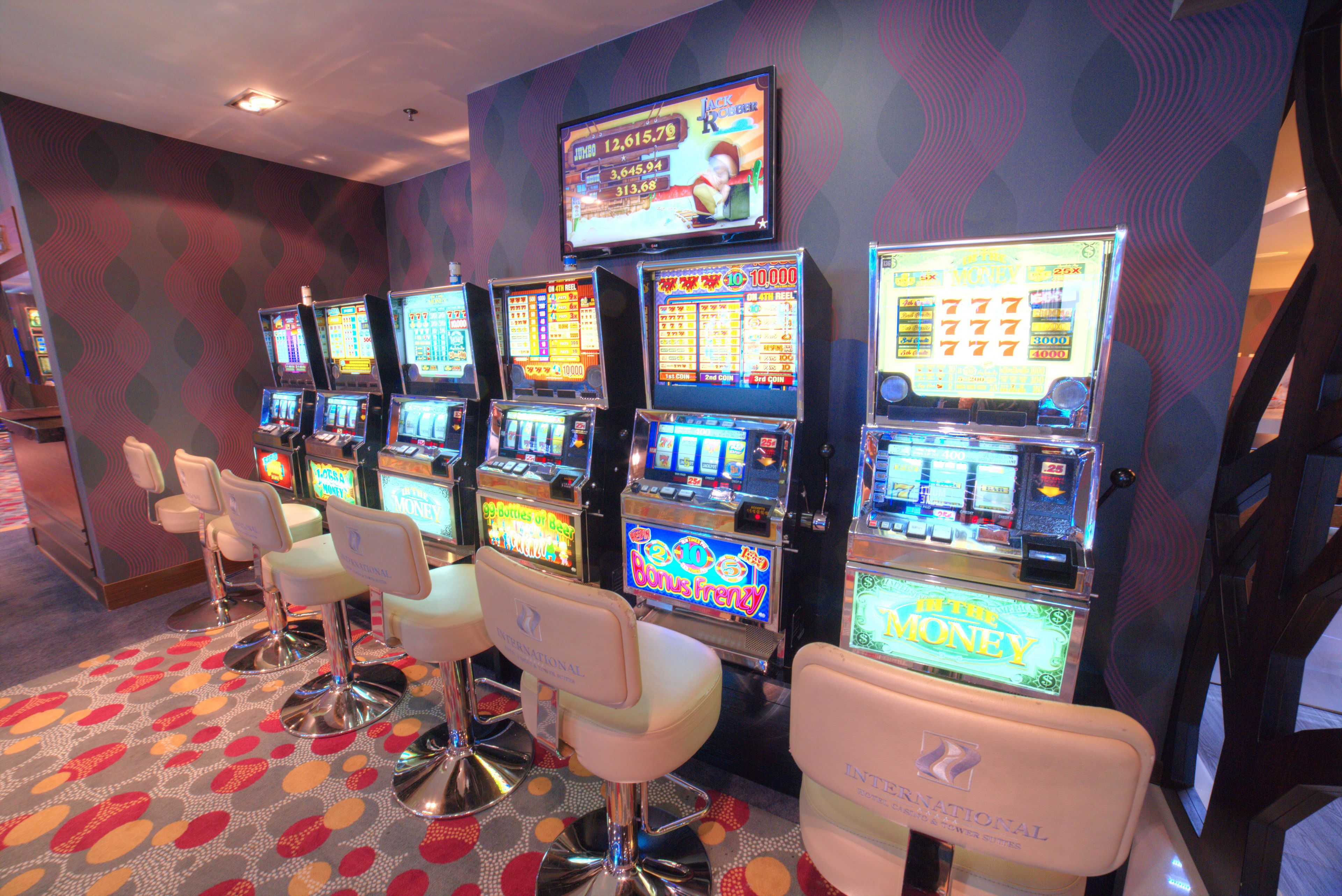 A row of slot machines with a television screen above them displaying game results.