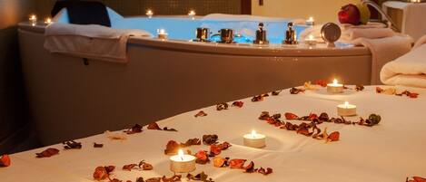 Un espacio de spa con una bañera, velas y flores secas dispuestas en el suelo.