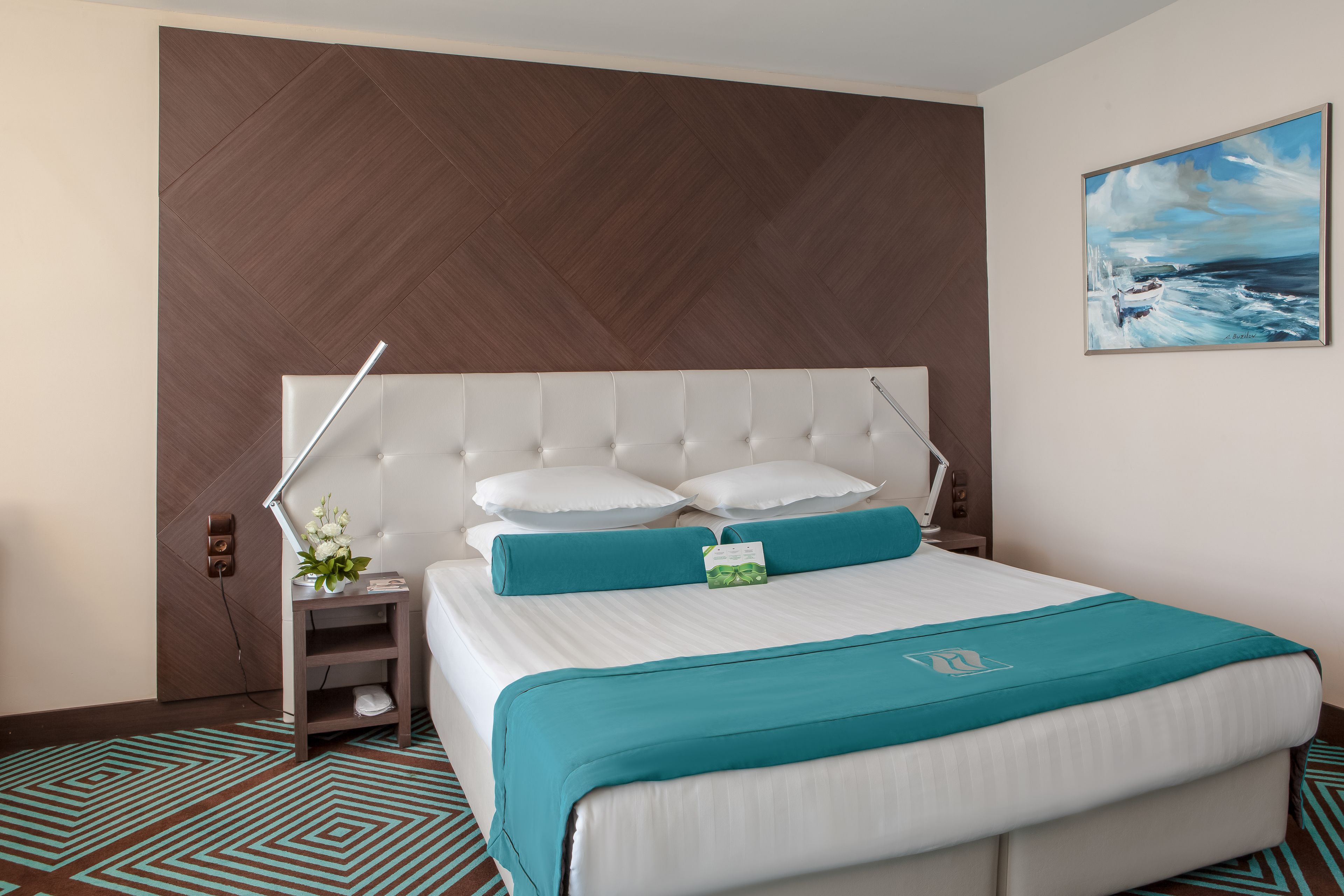 Habitación de hotel con una cama grande, una mesita de noche, una lámpara, un cuadro en la pared y un suelo con diseño.