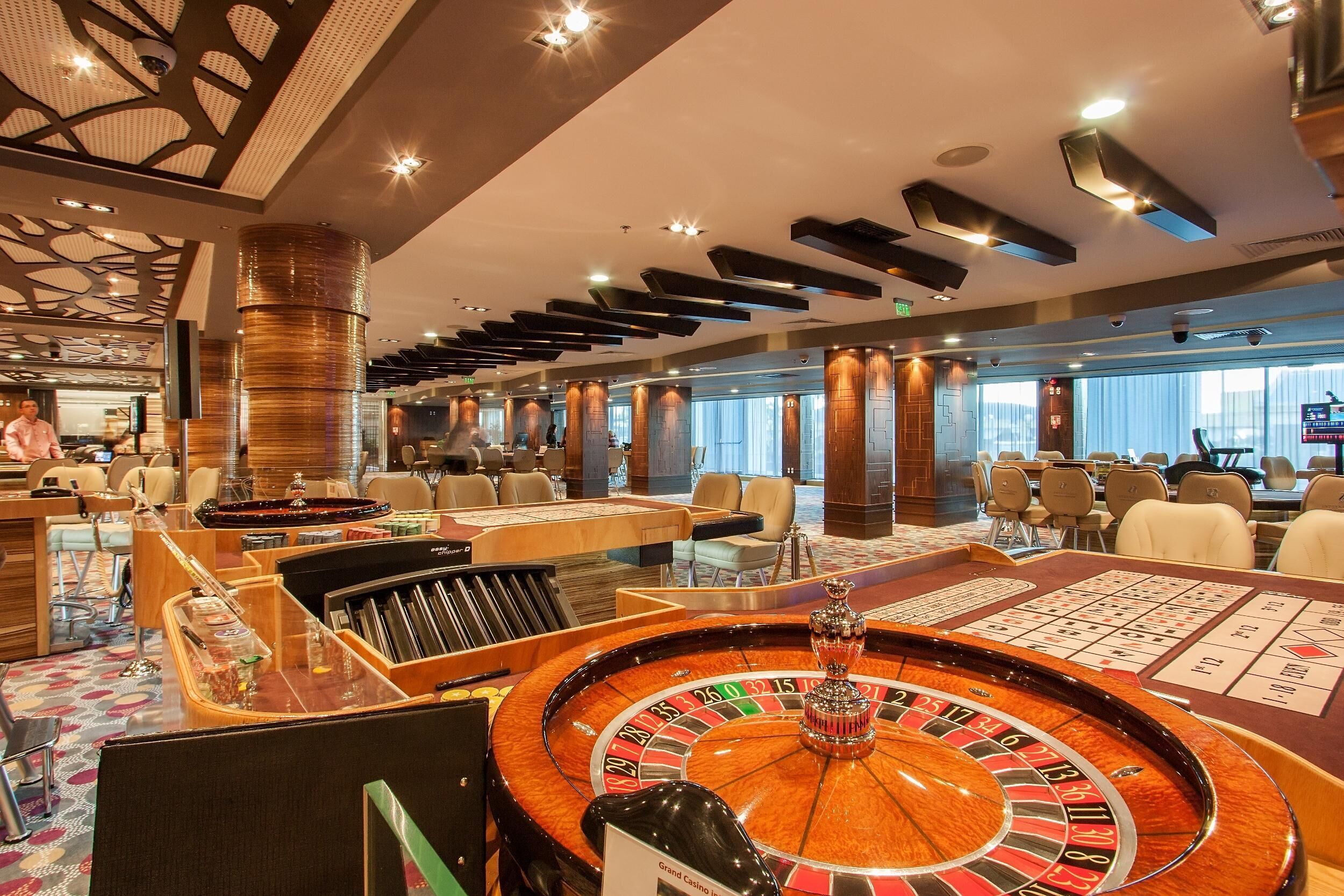 Un espace casino comprenant une table de roulette, des tables de jeux de cartes et un grand lustre.