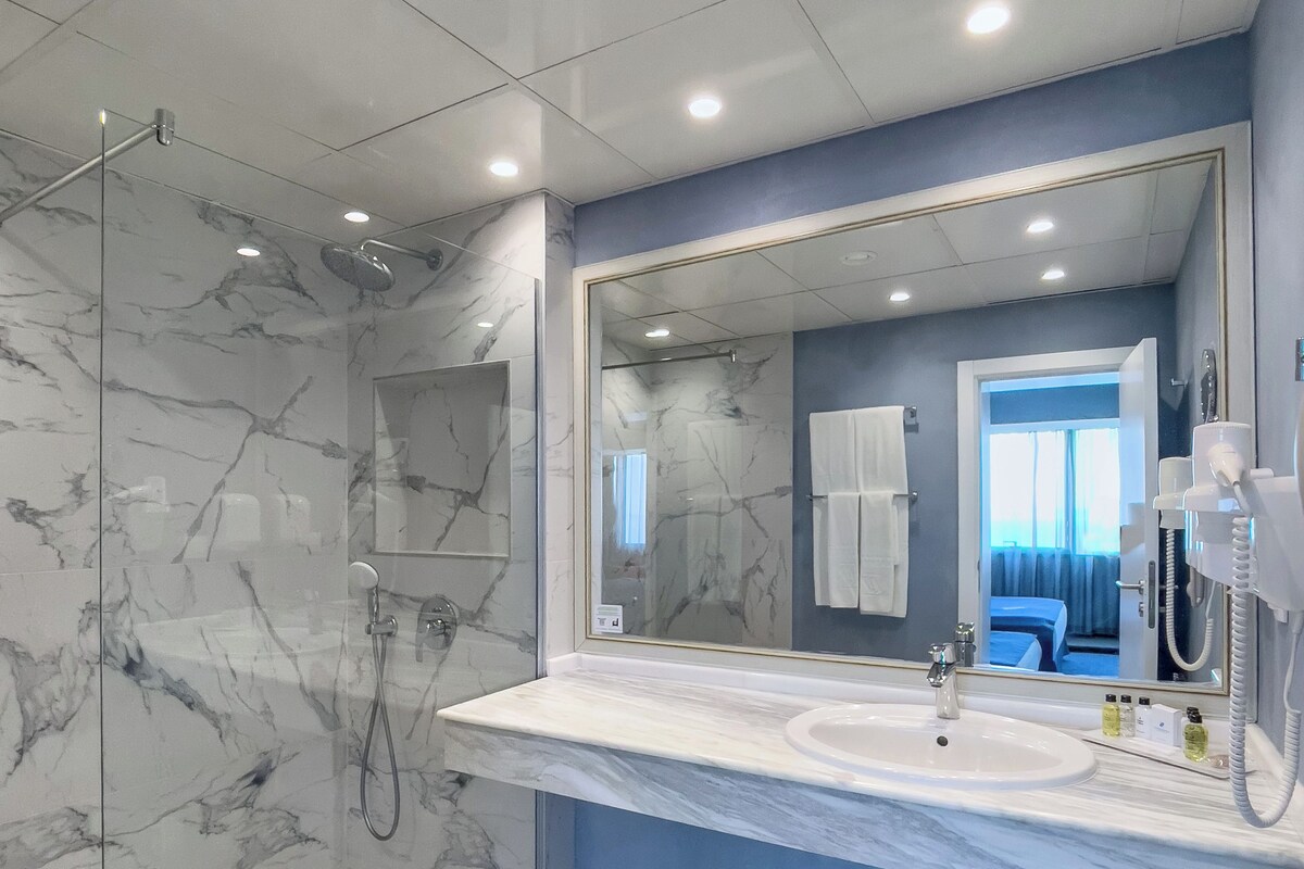 Une salle de bain moderne avec une douche en marbre, un grand miroir et un lavabo agrémenté d’un mur d’accent bleu.