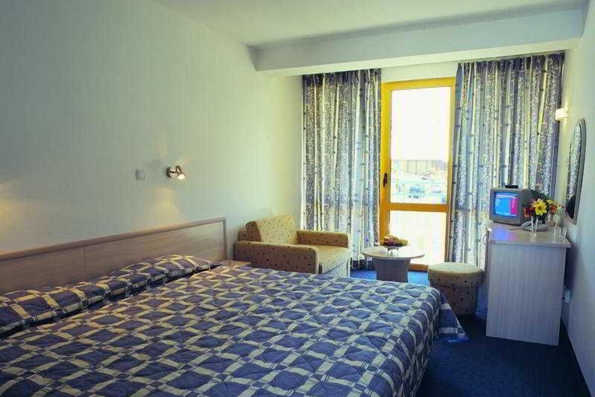 Een hotelkamer met twee bedden, een bureau, een stoel, een klein tafeltje en een televisie.
