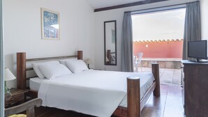A hotel room with a bed, a TV, a desk with a lamp, a chair, and a balcony with a view. - Hotel Villa Santo Antonio (Salvador)