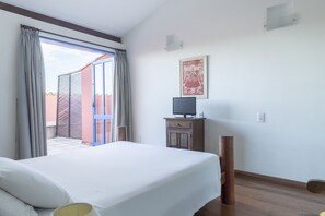 A hotel room with a bed, a television on a wooden cabinet, a sliding glass door to the outside, and a framed picture on the wall.