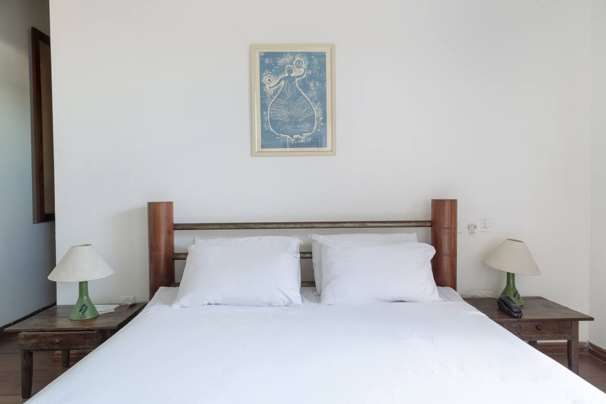 A neatly made bed with white linens, two bedside tables with lamps, and a framed artwork on the wall.