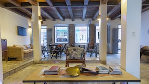 A spacious living area with a wooden table, books, and a decorative brass object. There are multiple chairs and a sofa in the background. - Hotel Villa Santo Antonio (Salvador)