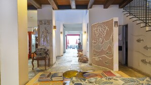 A hallway with a tiled floor, a table with books and a decorative bowl, a chair, and a wall with a fish mural. - Hotel Villa Santo Antonio (Salvador)