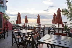 An outdoor seating area with wooden tables and chairs, orange umbrellas, and a view of the sea. - Hotel Villa Santo Antonio (Salvador)