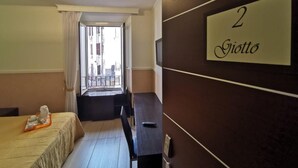 A hotel room with a bed, a desk, a chair, a TV, and a balcony with a view of buildings. The room has a sign indicating room number 2 and the name Giotto. - Mocenigo Vatican Suites (Rome)