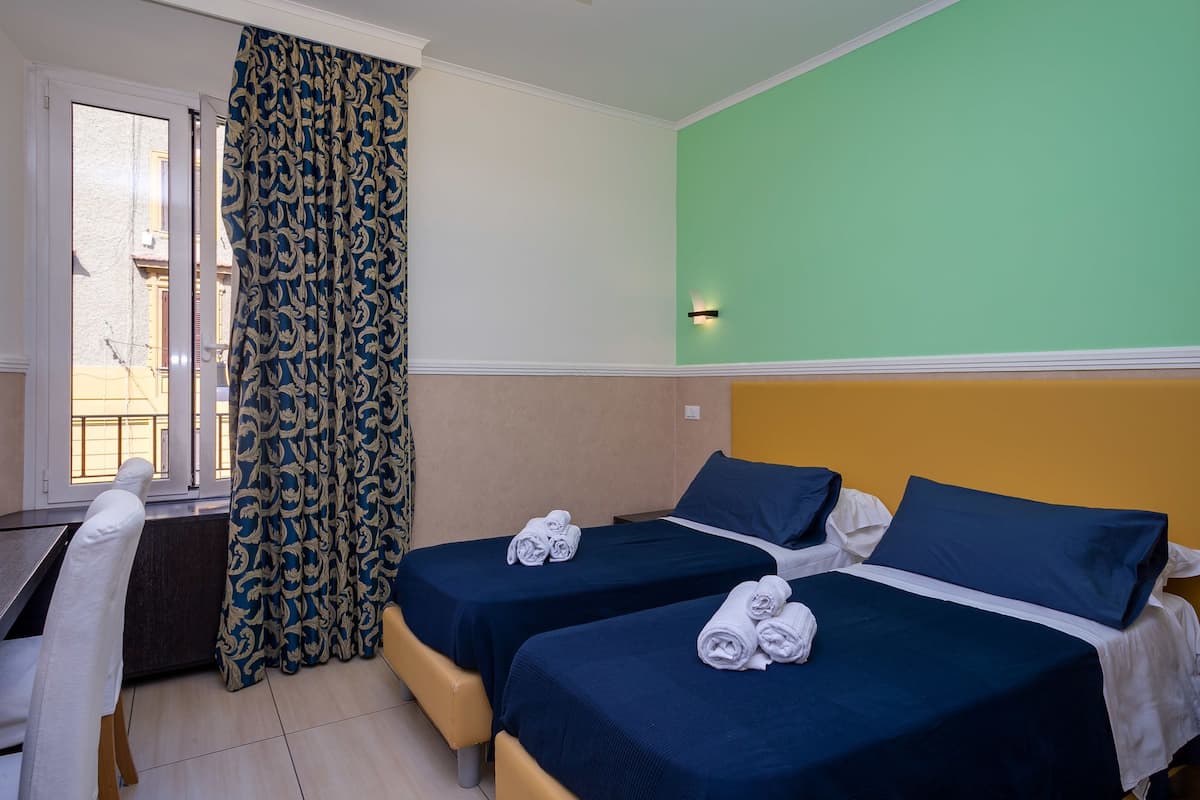 A hotel room with two beds, a desk, and a window with curtains.
