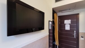 A hotel room with a large flat-screen TV mounted on the wall, a dark wooden door with a lock, and a small table in the corner. - Mocenigo Vatican Suites (Rome)
