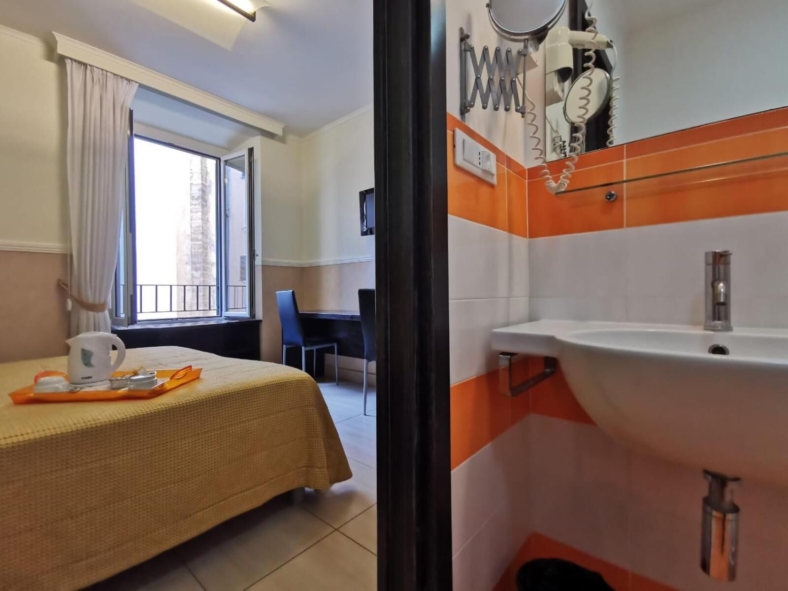 A hotel room with a bed, a desk, a window with curtains, and a bathroom with a sink and mirror.
