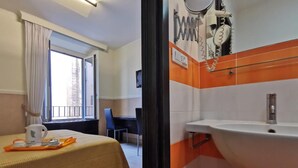 A hotel room with a bed, a desk, a window with curtains, and a bathroom with a sink and mirror. - Mocenigo Vatican Suites (Rome)