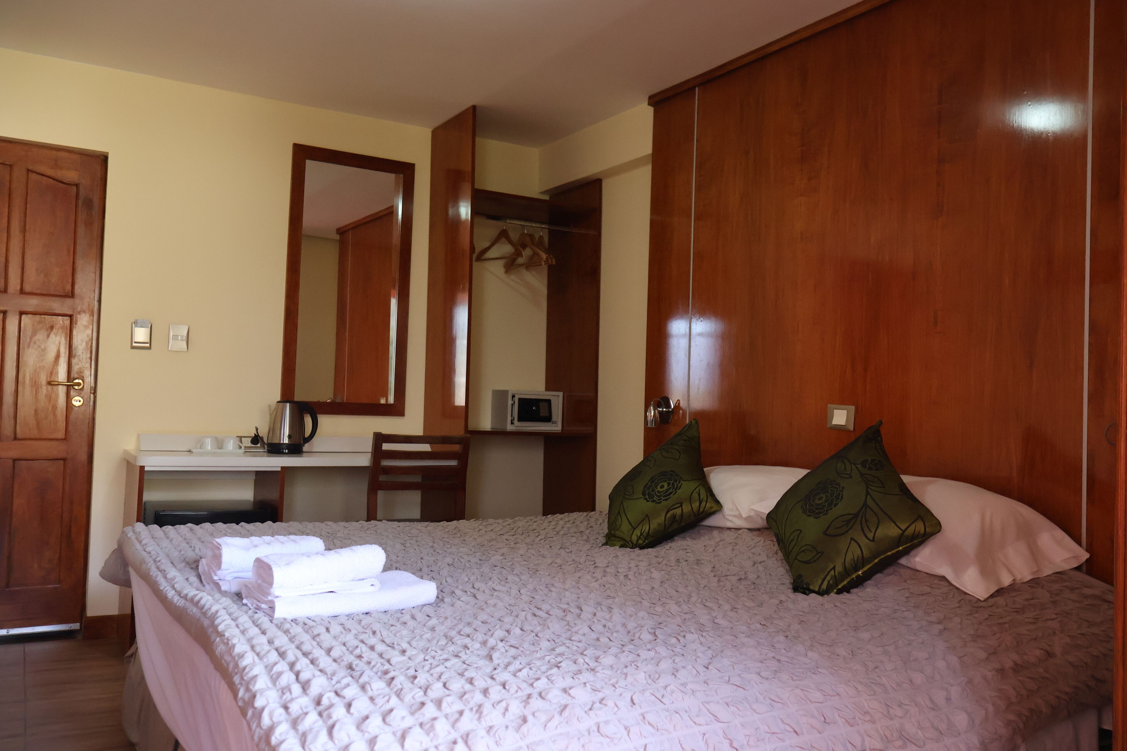 Quarto com cama, guarda-roupa de madeira, escrivaninha com chaleira e espelho.