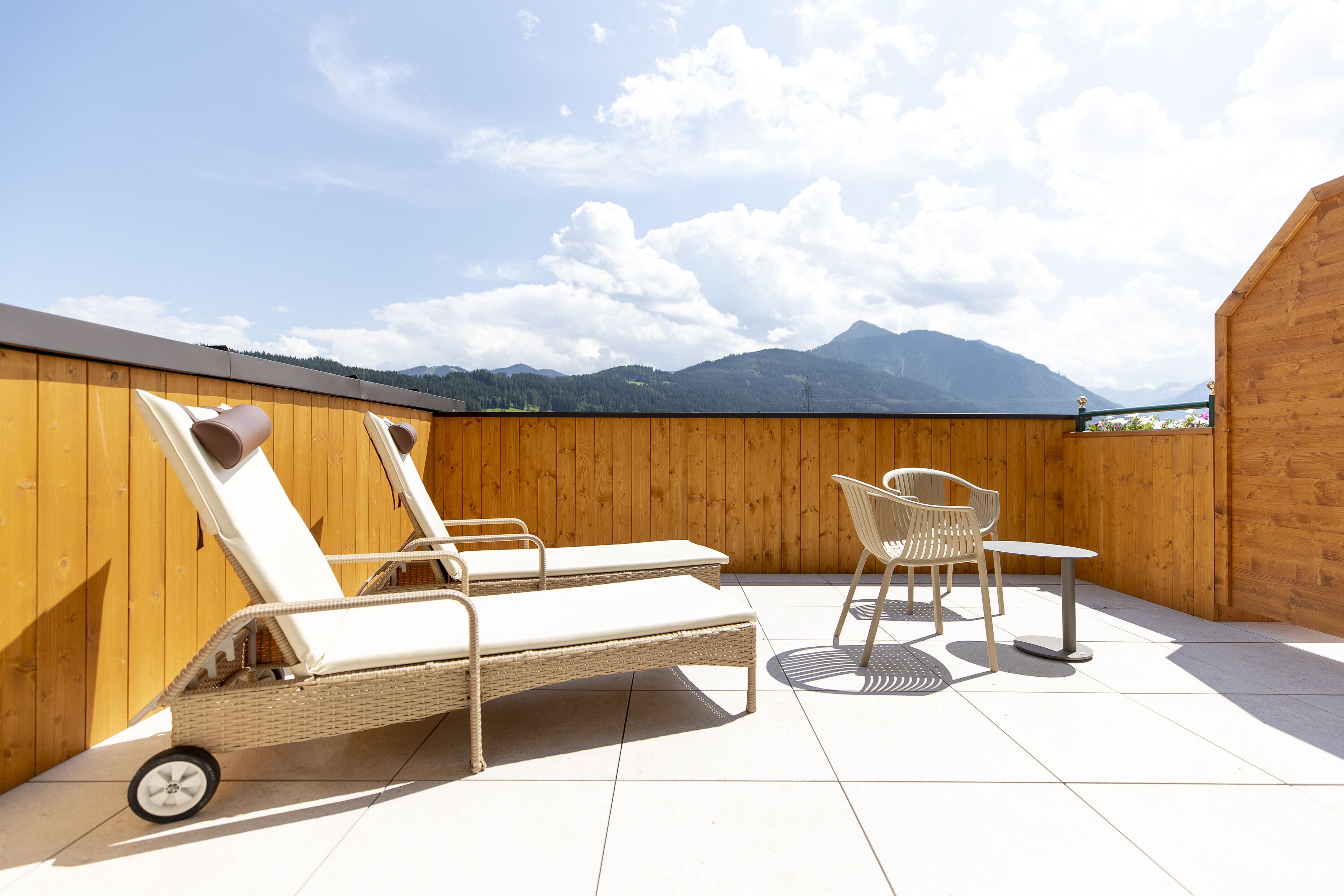 A rooftop terrace with two lounge chairs, a table, and a chair.