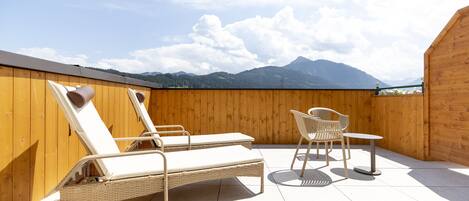 A rooftop terrace with two lounge chairs, a table, and a chair.