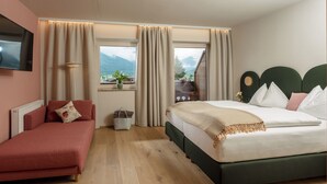 A bedroom with a bed, a sofa, a TV, and a window with curtains. - Hotel Felsenhof (Flachau)