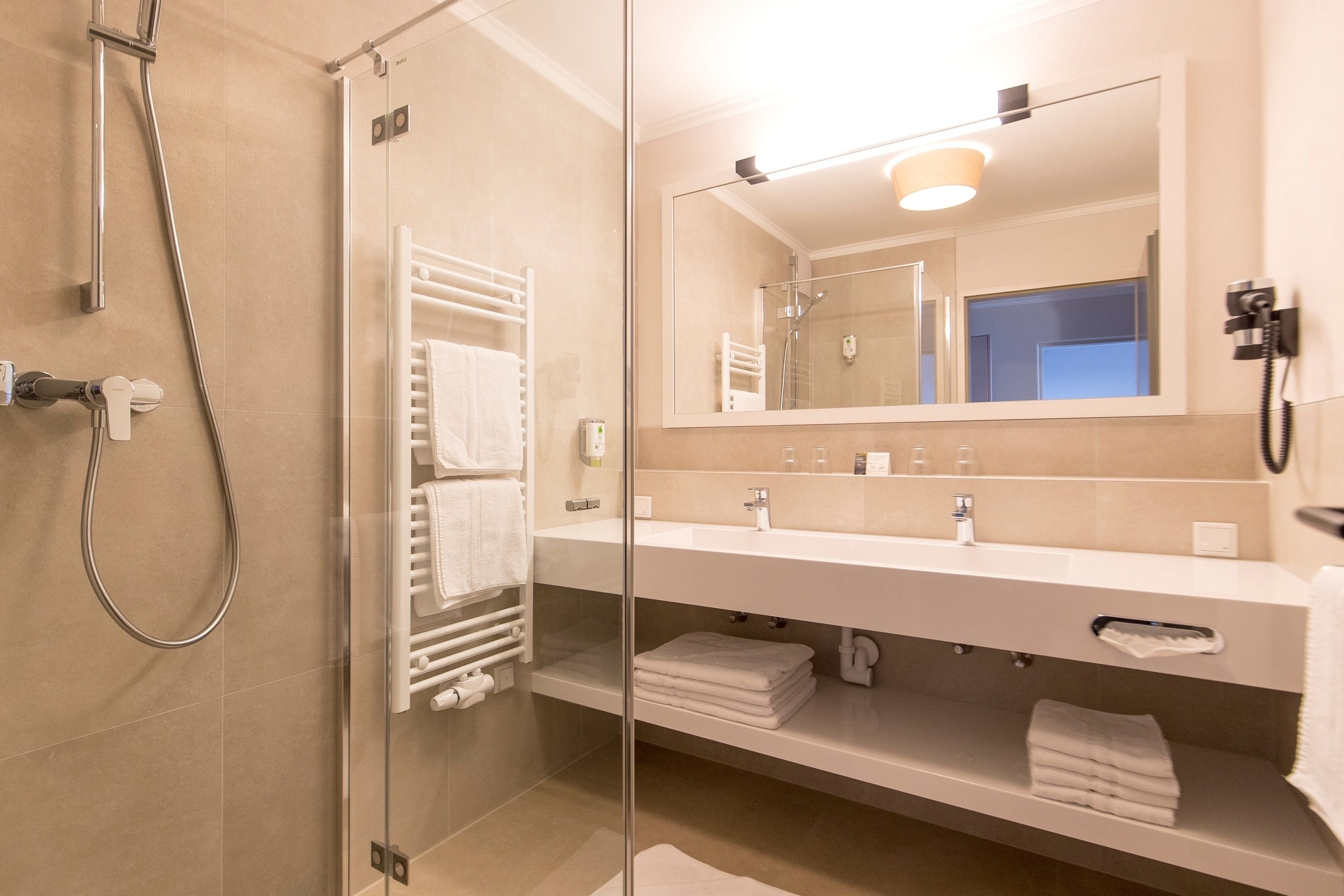 Ein modernes Badezimmer mit einer Glaskabinent Dusche, einem großen Spiegel und einem weißen Waschtisch mit Handtuchhalter.
