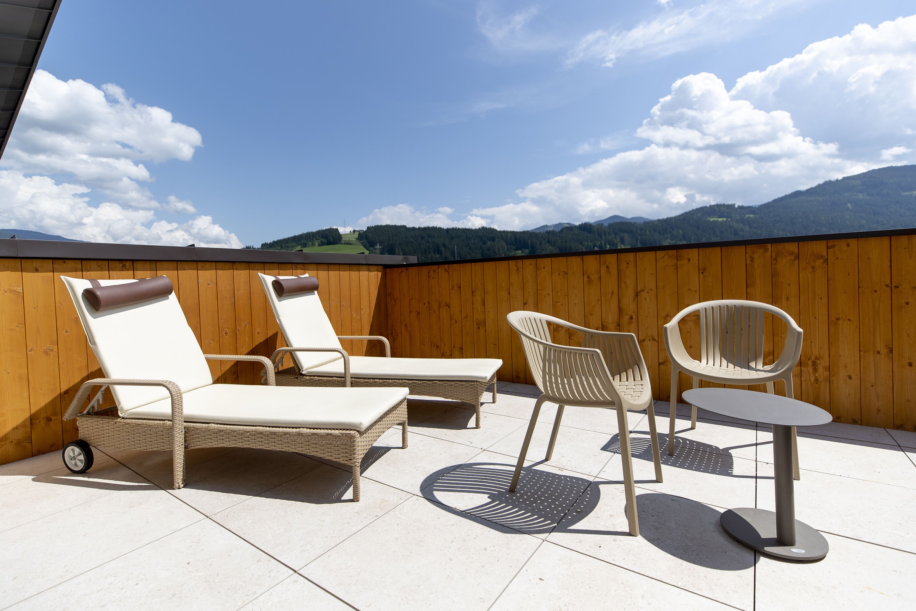 Terraza en la azotea con sillones de mimbre y una mesa, con vistas a un paisaje montañoso.