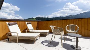 Terraza en la azotea con sillones de mimbre y una mesa, con vistas a un paisaje montañoso.