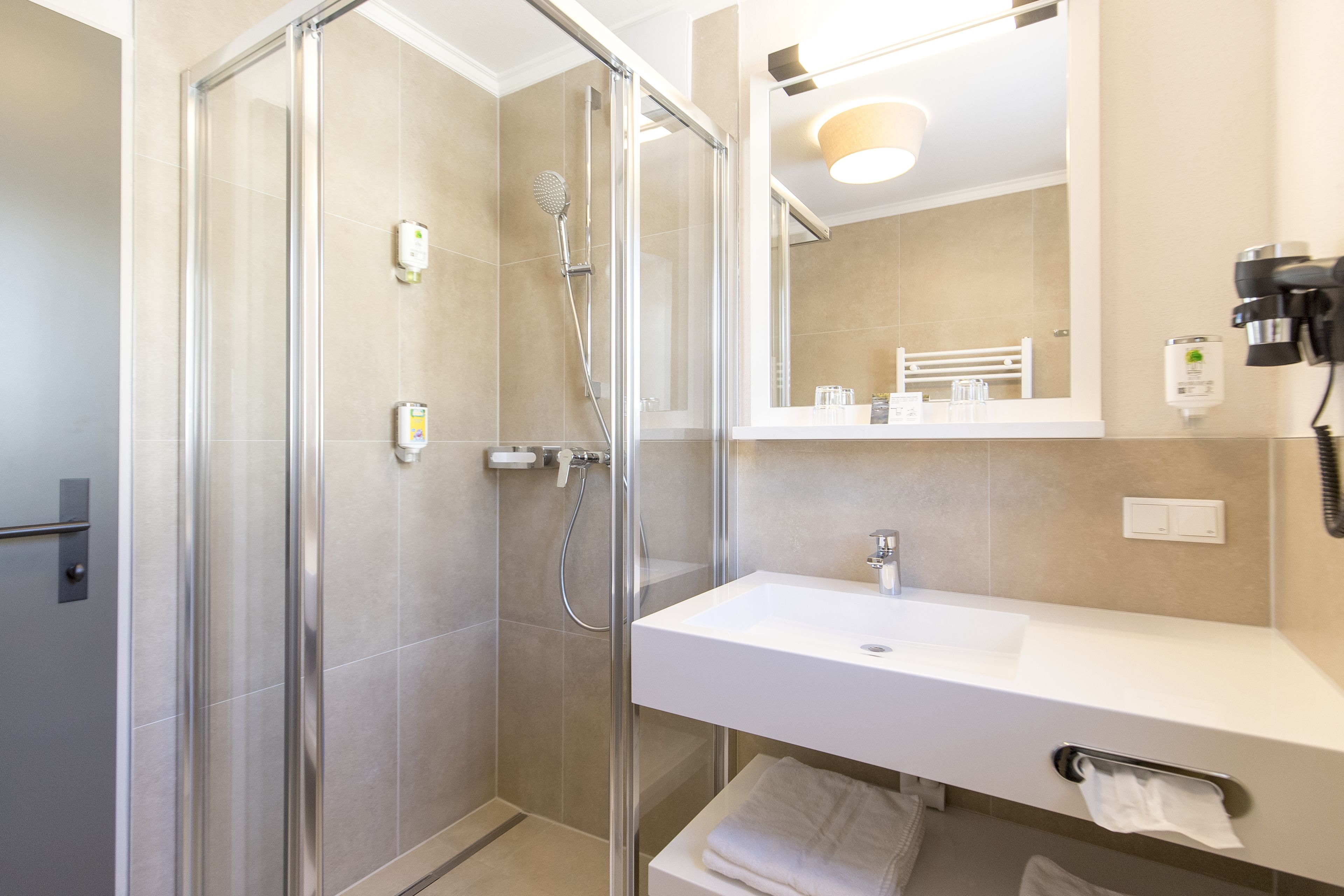 Een moderne badkamer met een douchecabine van glas, een wit wastafelmeubel en een spiegel erboven.