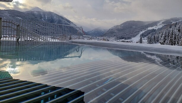 A glass-bottomed infinity pool with a metal railing, surrounded by snow-covered mountains and a clear sky. - Hotel Felsenhof (Flachau)