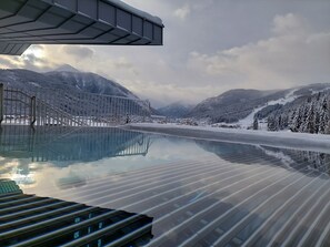 A glass-bottomed infinity pool with a metal railing, surrounded by snow-covered mountains and a clear sky. - Hotel Felsenhof (Flachau)