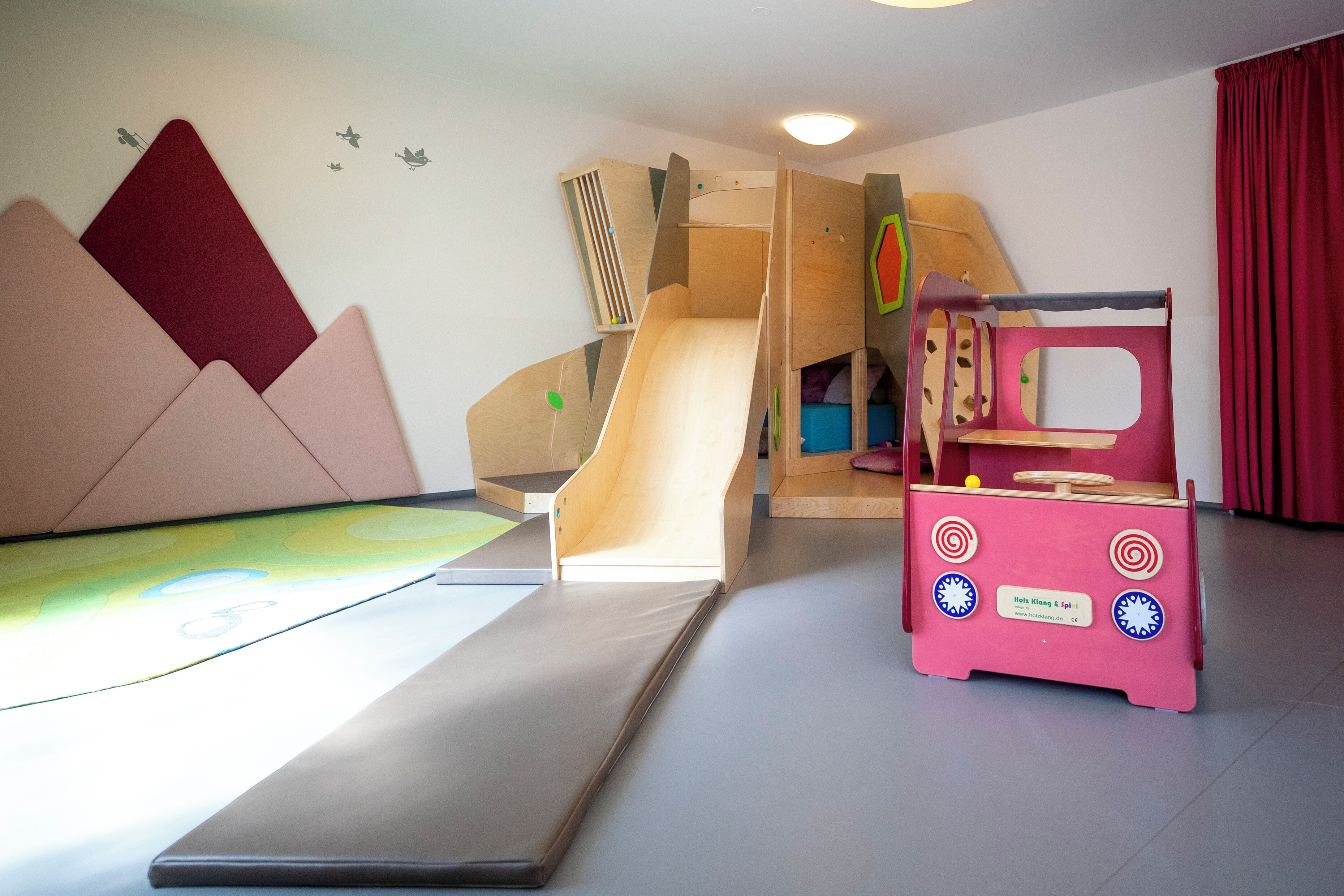 Ein Spielbereich mit Rutsche, Kletterwand und einem rosa Spielhaus.
