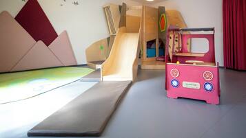 Ein Spielbereich mit Rutsche, Kletterwand und einem rosa Spielhaus.