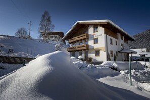A two-story building with a balcony, surrounded by snow. - Hotel Felsenhof (Flachau)