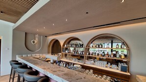 A bar area with a long counter, multiple stools, and shelves stocked with bottles and glasses. - Hotel Felsenhof (Flachau)