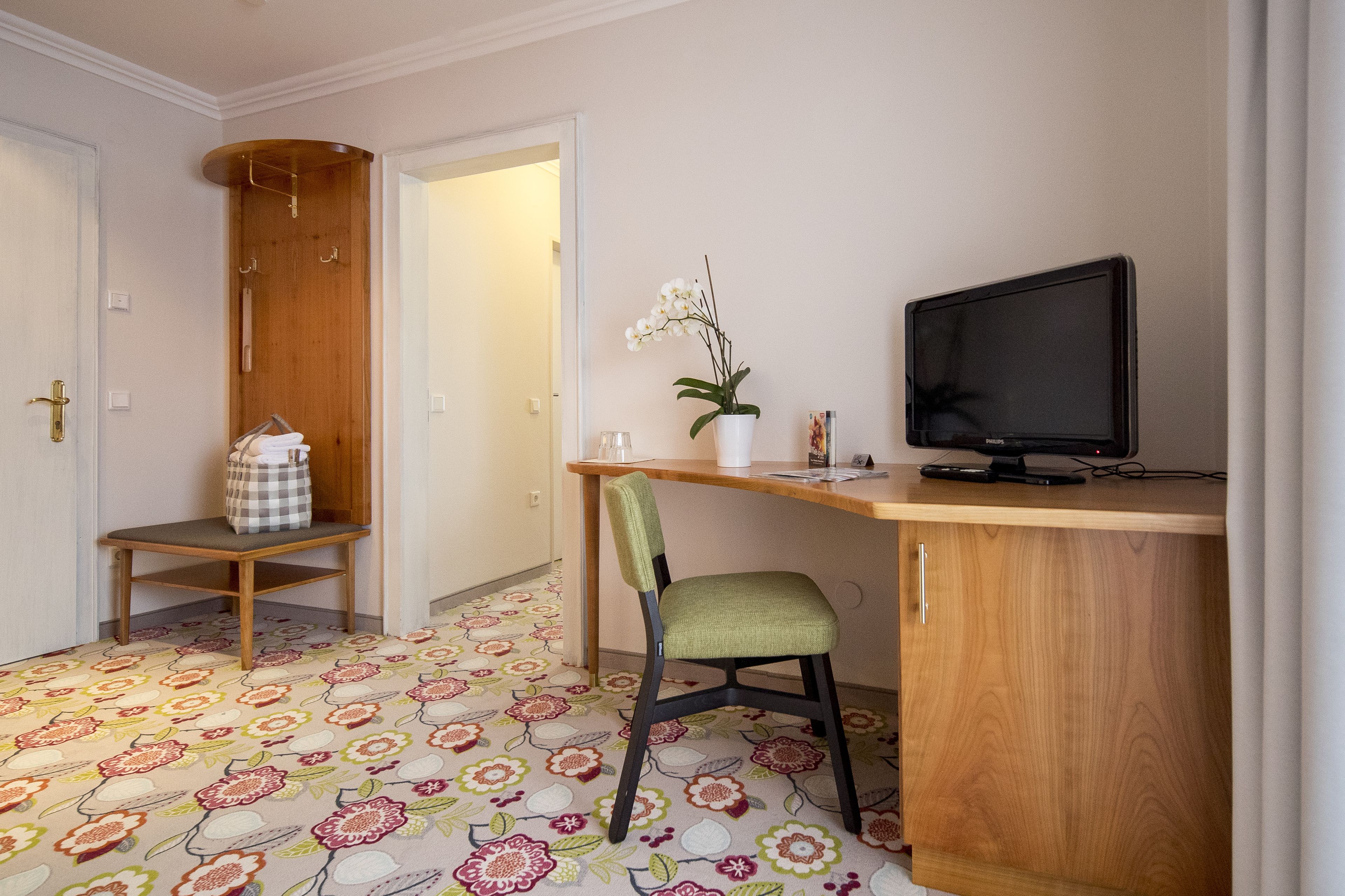 A small room with a wooden desk, a chair, a television, and a patterned carpet.