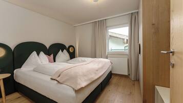Ein ordentlich eingerichtetes Schlafzimmer mit Bett, Nachttischen, einem Fenster mit Vorhängen und einer Heizung.