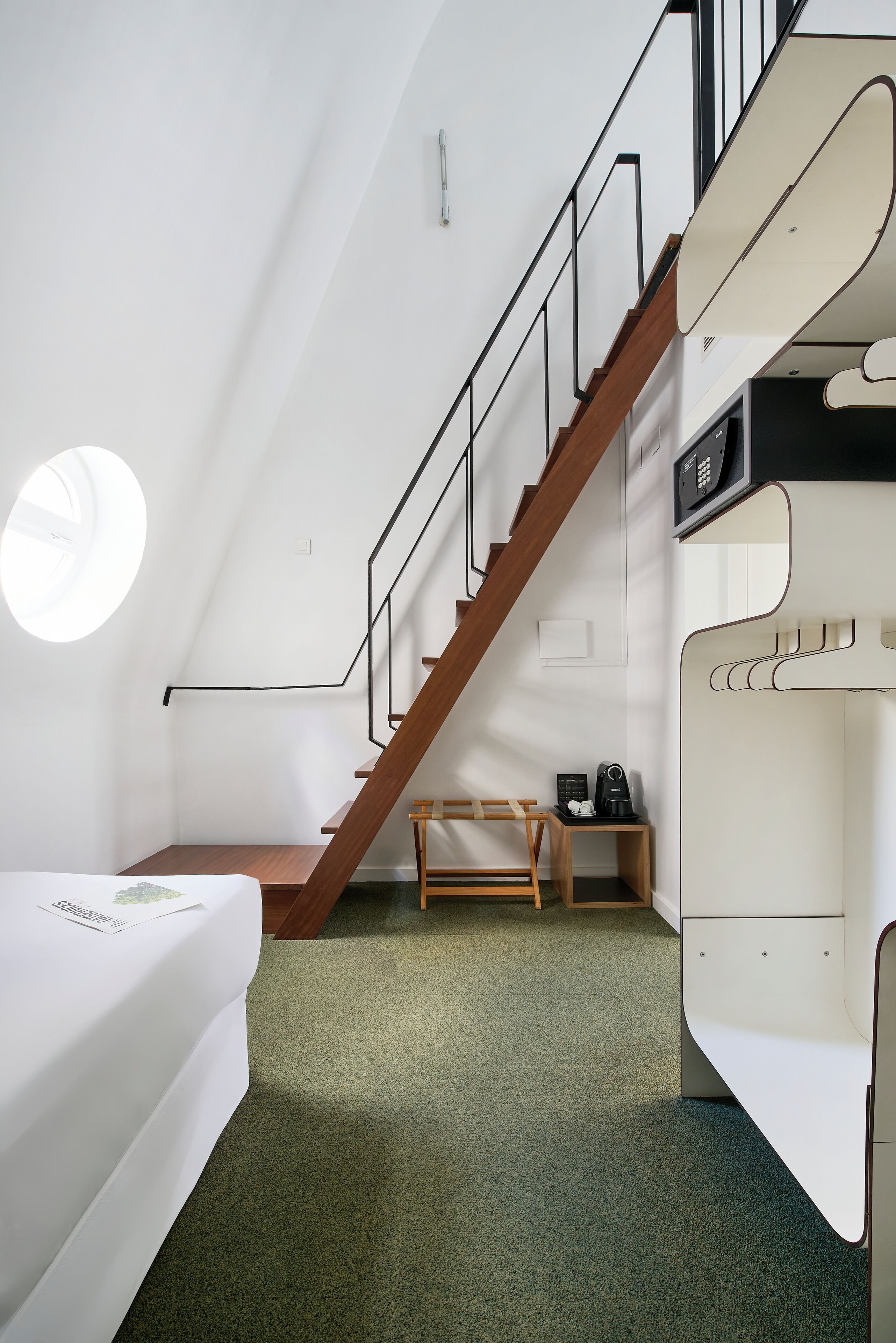 A modern room with a bed, a small table, a chair, a coat rack, and a staircase.