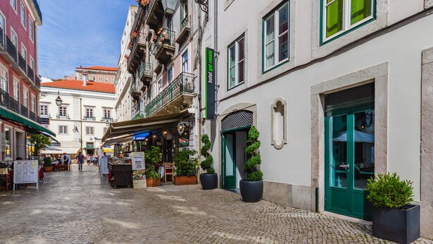 Una calle adoquinada flanqueada por edificios, incluyendo un hotel con puerta verde y un letrero que dice "hotel gel rosso".